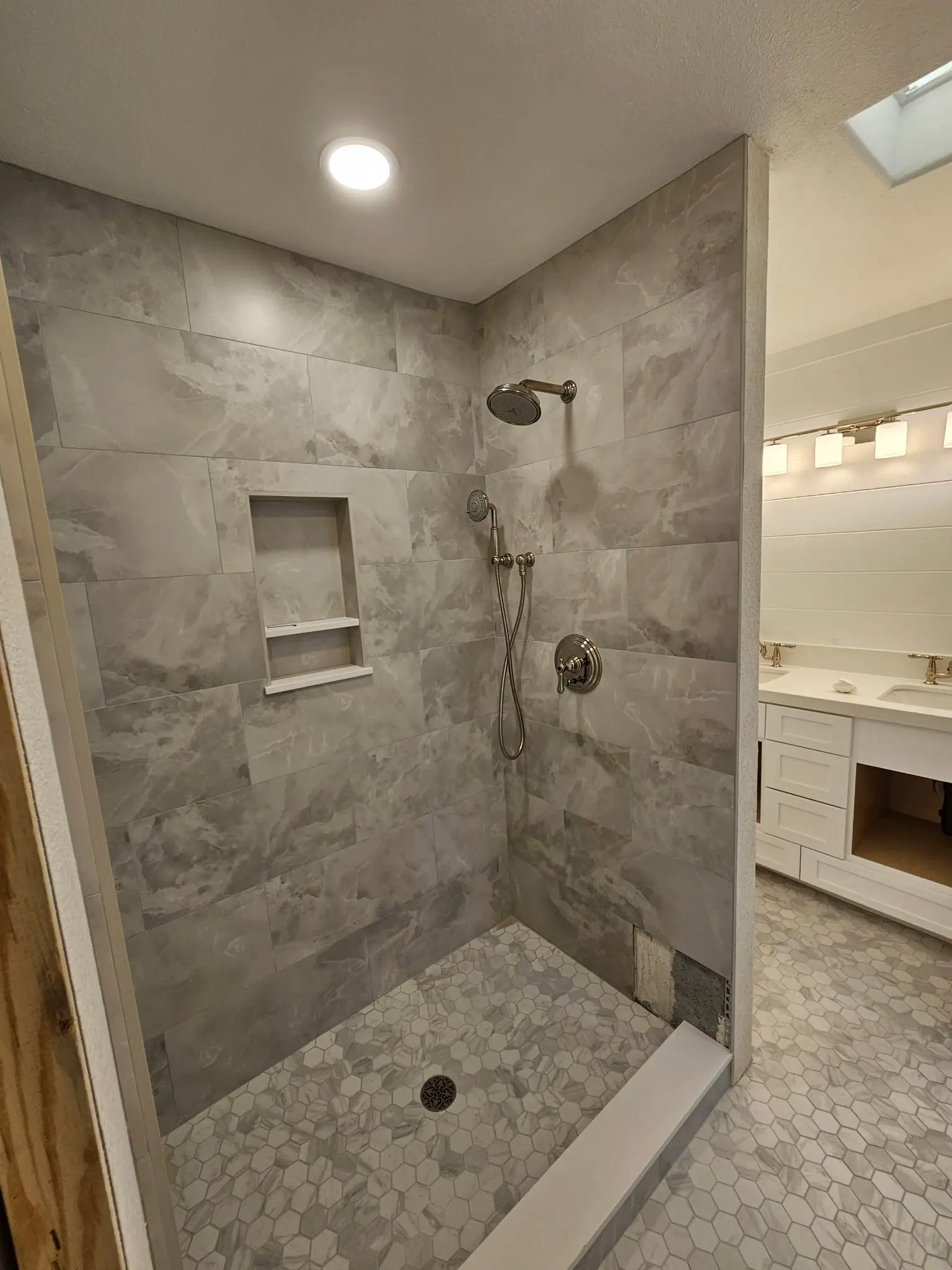 Finished walk-in shower in large-format marble tile with a recessed niche